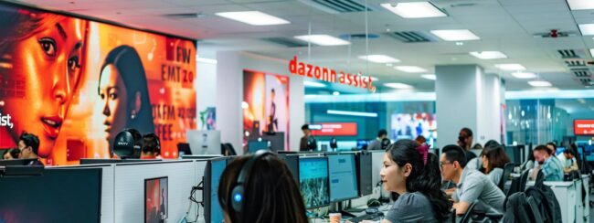 a bustling call center filled with focused employees at their desks, surrounded by vibrant wall art featuring "dazonn assist," highlighting a dynamic and collaborative atmosphere aimed at fostering agent competence.