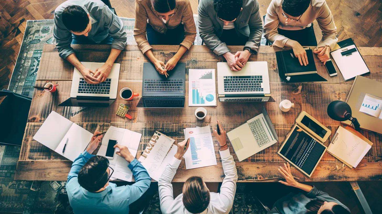 Group of professionals collaborating around a wooden table with laptops and documents, discussing call center outsourcing strategies and operational transition.