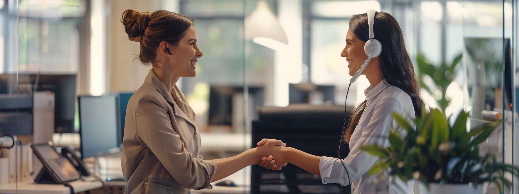 Two women shaking hands in a modern office setting, one wearing a headset, symbolizing collaboration and effective communication in lead generation efforts.