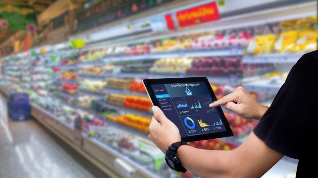 Person using a tablet to display smart retail management analytics in a grocery store, surrounded by colorful produce.